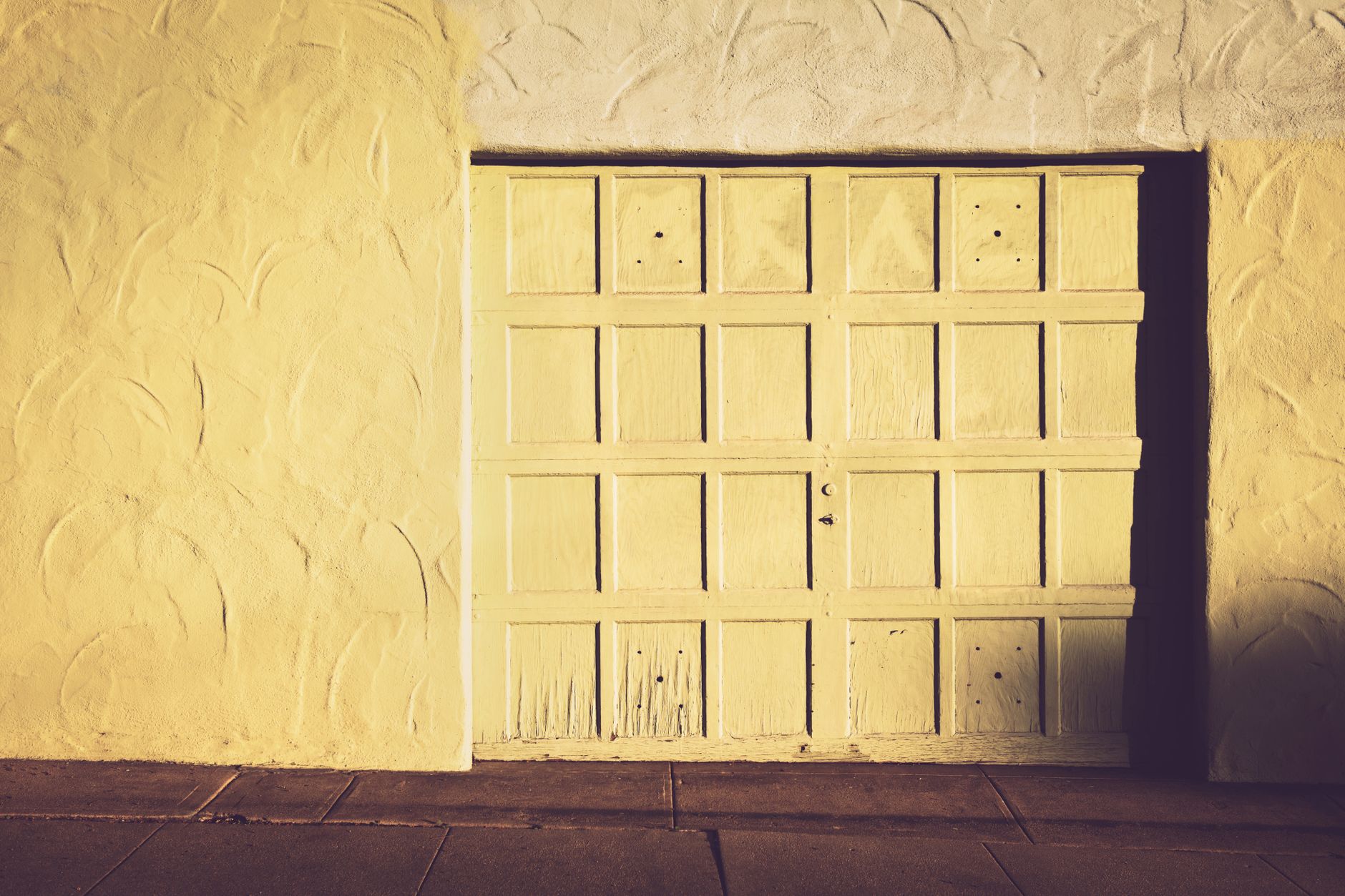 A vintage wooden garage door set against a textured wall in warm, muted tones in Long Beach, CA